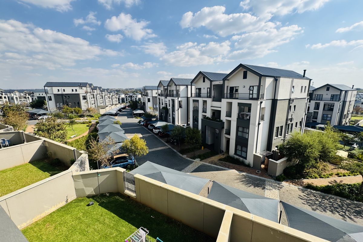 An elevated aerial view of a modern residential apartment complex featuring paved driveways, covered parking bays, and landscaped communal garden areas.