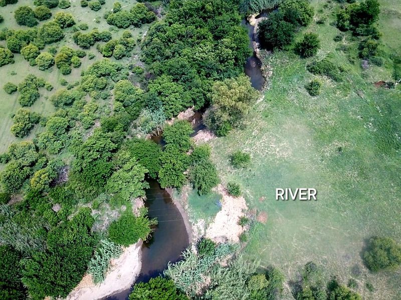 Aerial view of the farm property featuring a natural river flowing through the lush green landscape and indigenous vegetation.