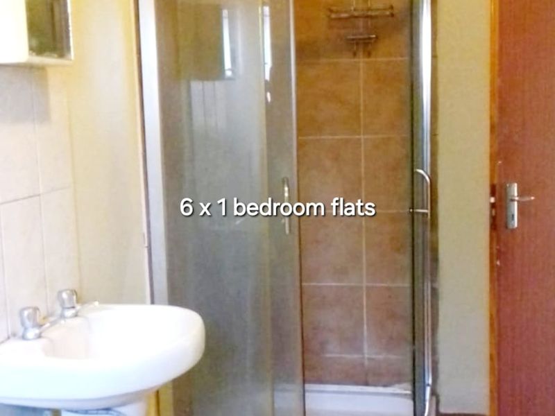 A functional bathroom featuring a corner shower enclosure with glass doors, a pedestal basin, and tiled flooring.