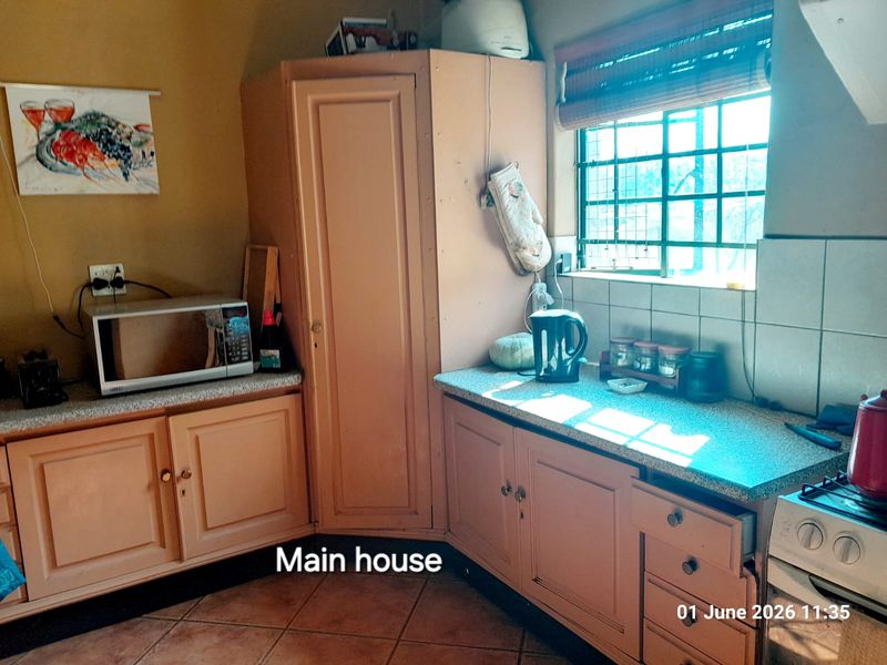 A dated kitchen area featuring built-in wooden cabinetry, tiled flooring, and a window with security bars, providing a functional prep space.