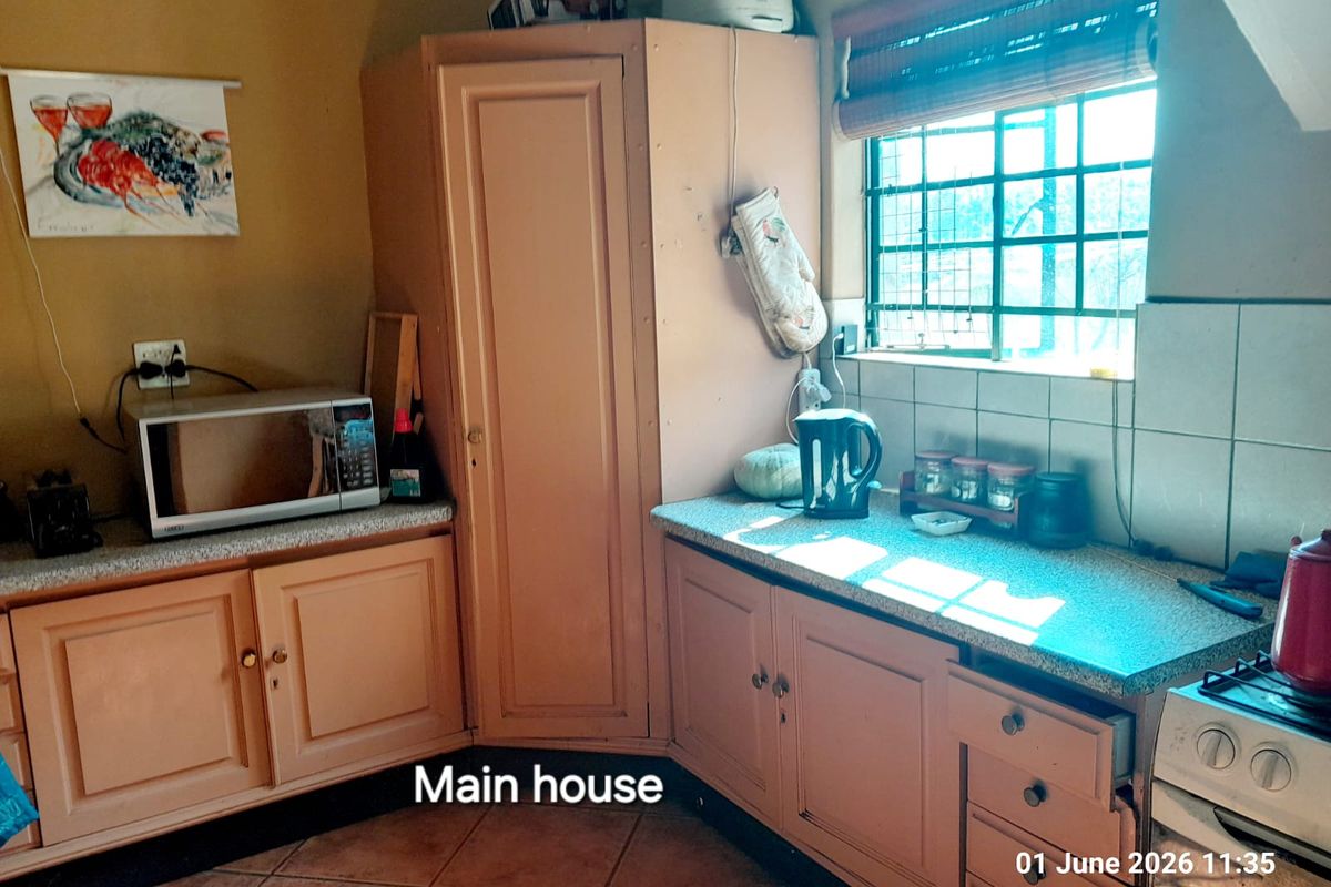 A dated kitchen area featuring built-in wooden cabinetry, tiled flooring, and a window with security bars, providing a functional prep space.