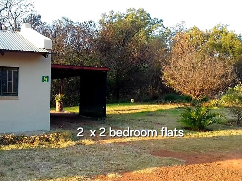 Exterior view of a farm flat featuring a covered carport area and surrounding natural landscape.