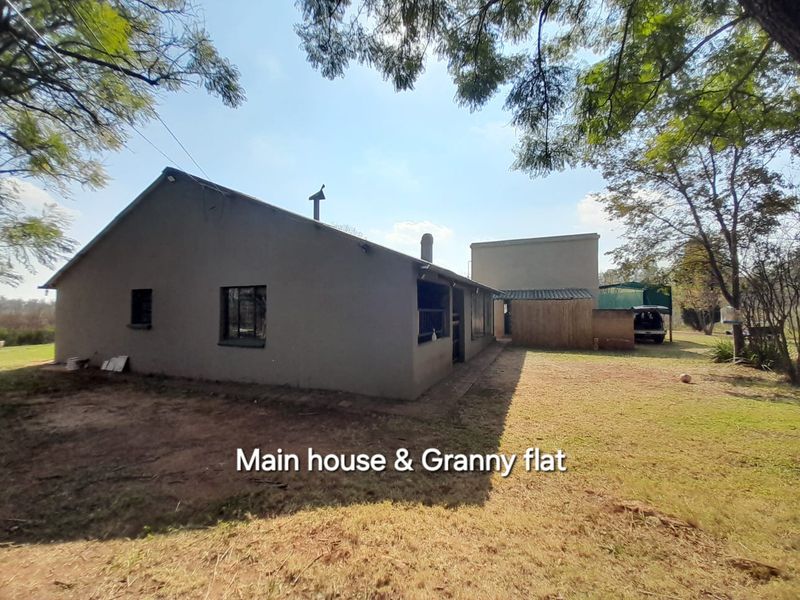Exterior view of the main farmhouse and attached granny flat, featuring a simple structure set within a spacious rural garden area.