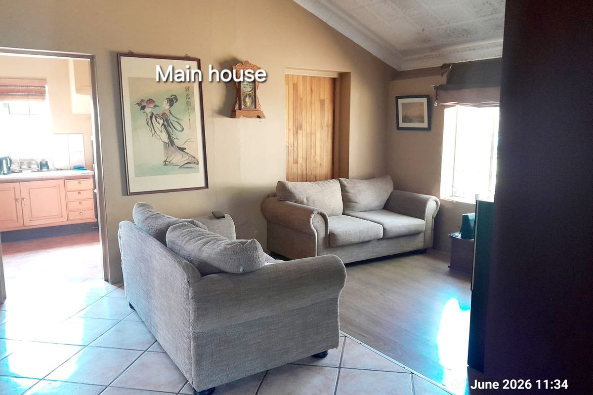 A living room area featuring tiled flooring, vaulted ceilings, and a view into the adjacent kitchen space.