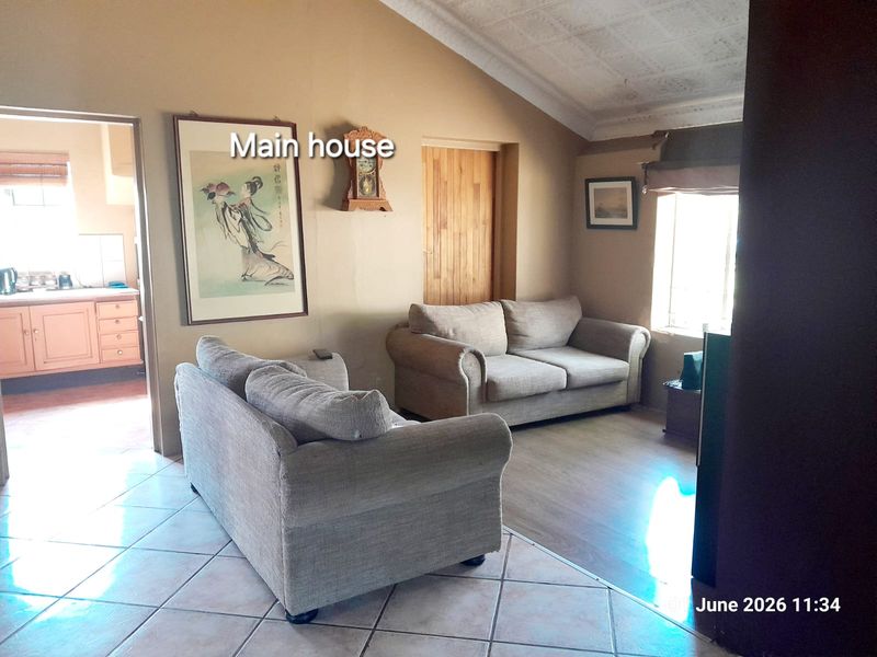 A living room area featuring tiled flooring, vaulted ceilings, and a view into the adjacent kitchen space.