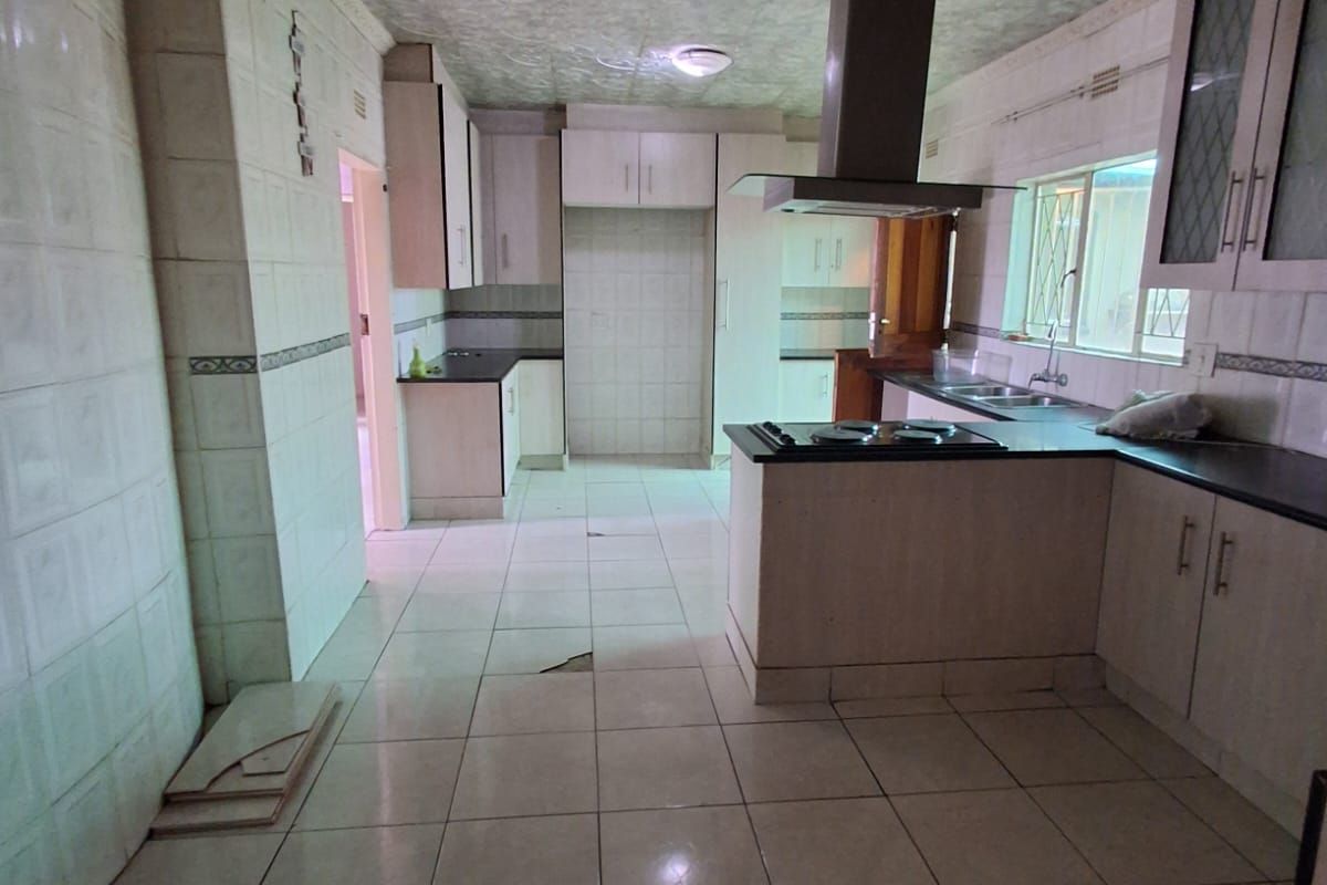 A spacious kitchen featuring built-in cabinetry, a central extractor fan, and tiled flooring, currently requiring maintenance and cosmetic updates.