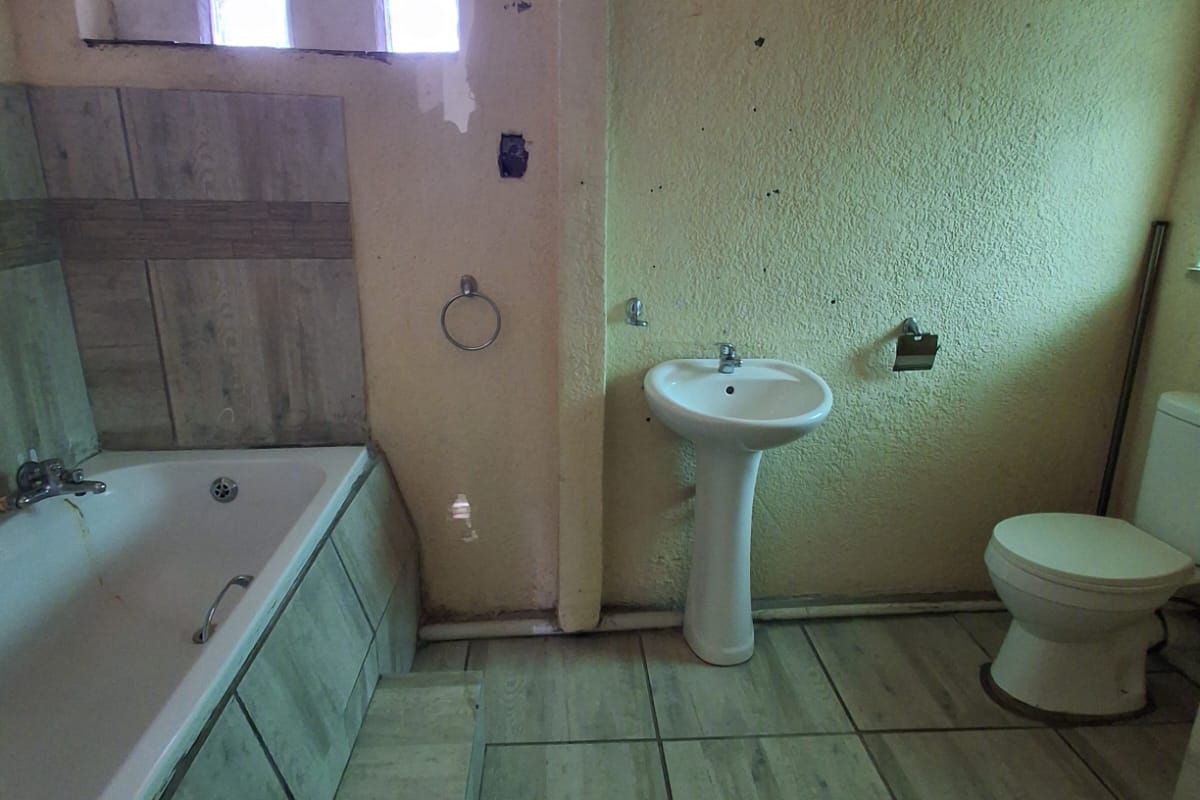 A dated bathroom featuring a built-in bathtub with tiled surround, pedestal basin, and toilet, requiring cosmetic updates and wall repairs.