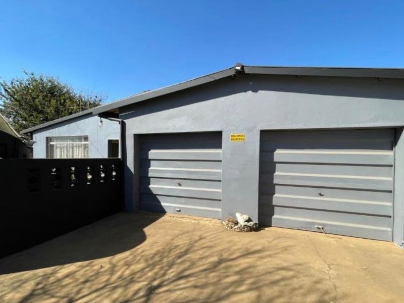 A double garage with grey doors and a concrete driveway, featuring a surrounding perimeter wall.