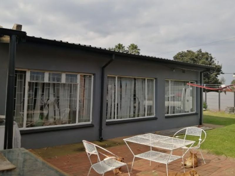 Rear view of the house featuring a brick patio, grey exterior walls, and large windows with security bars.