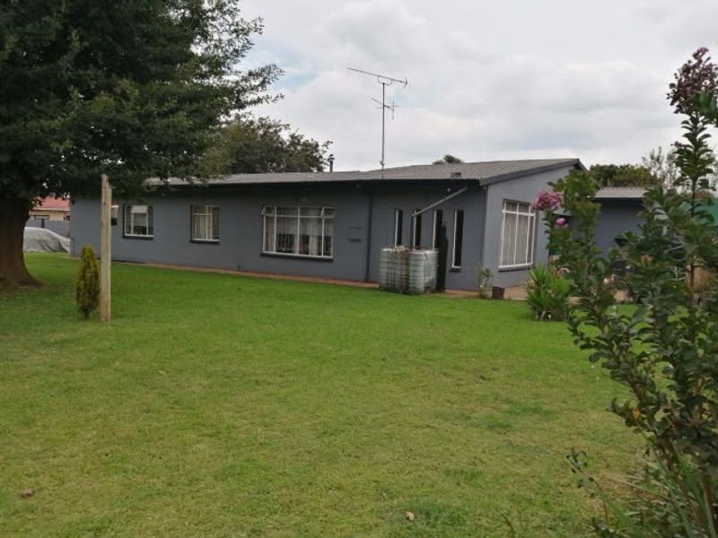 Rear view of a single-story house featuring a large lawn, metal roofing, and aluminium window frames.