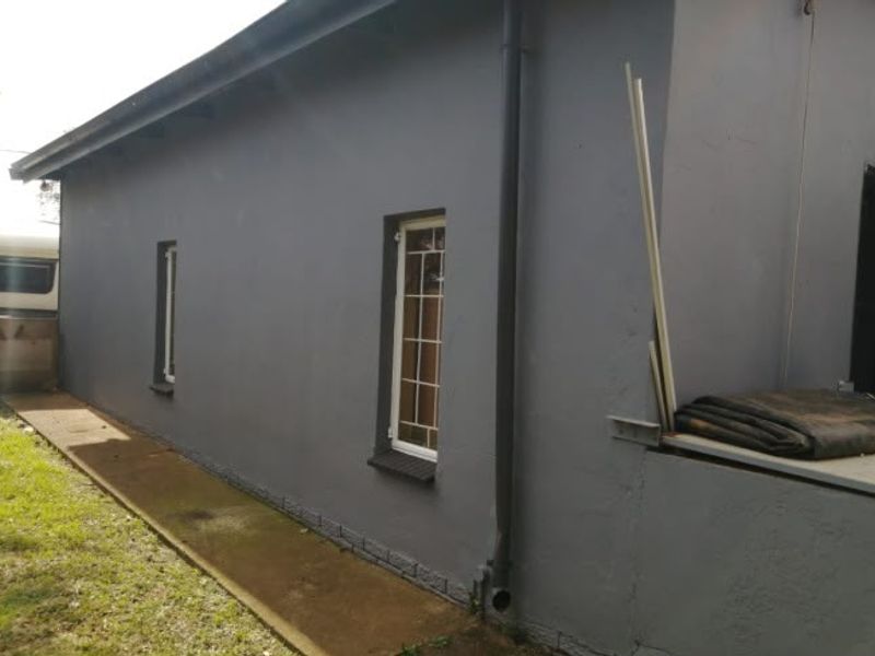 A side view of the house exterior featuring a painted grey facade, concrete pathway, and installed downpipe.