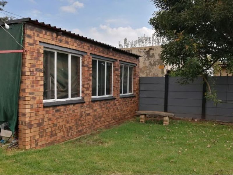 Rear view of a face brick outbuilding featuring aluminium windows, a corrugated roof, and a private garden area with a precast concrete boundary wall.