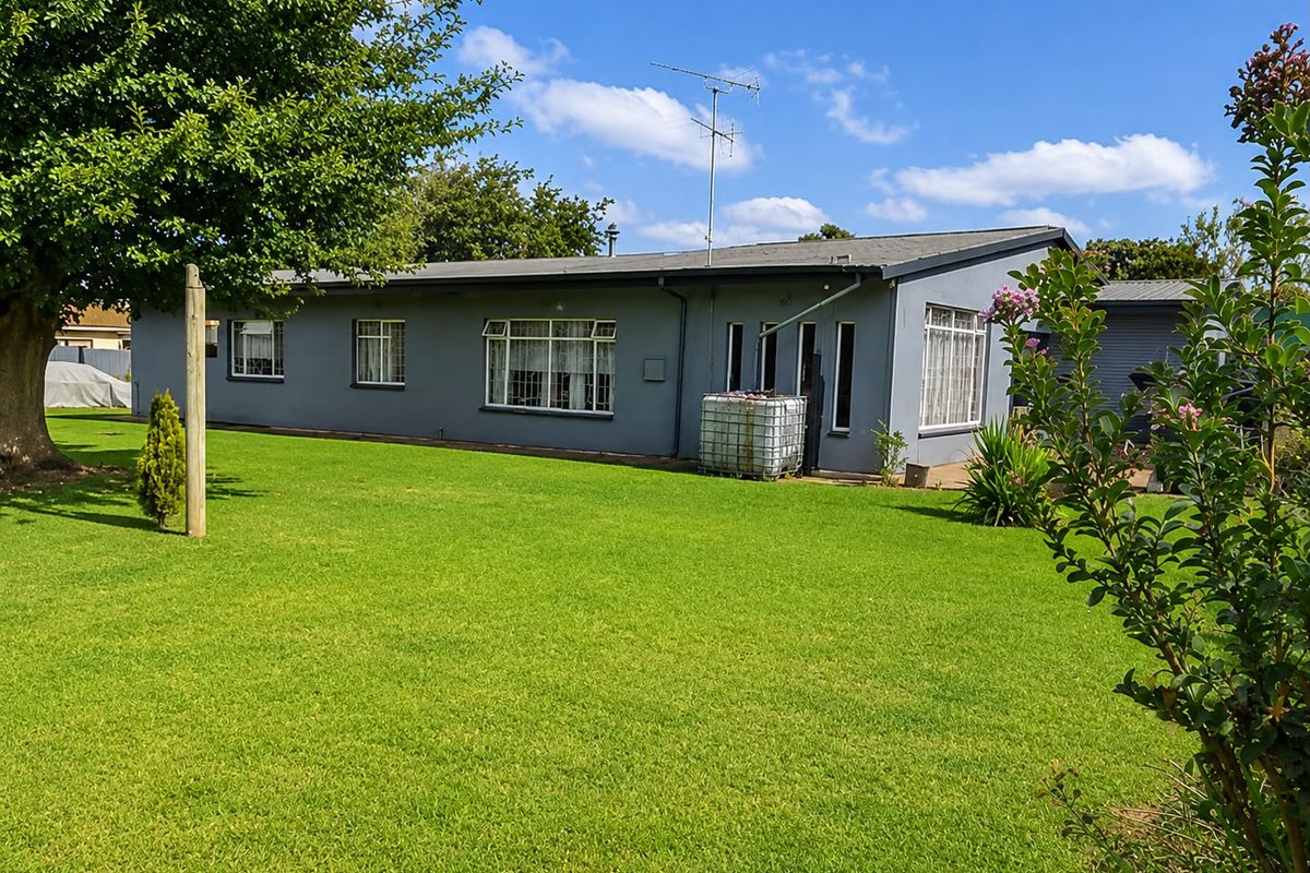 A view of the rear exterior of the house featuring a well-maintained lawn, mature trees, and a grey painted facade with aluminium windows.