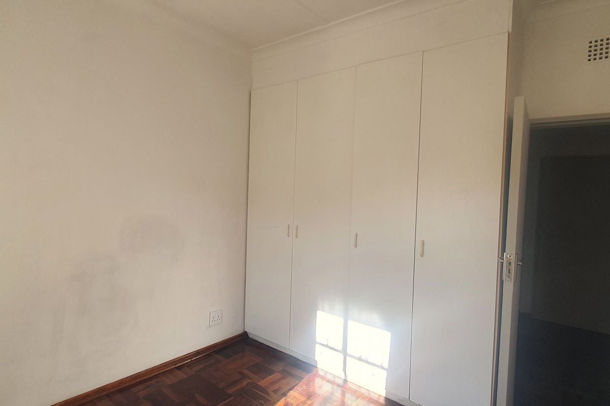 A bedroom featuring built-in cupboards and parquet flooring, offering a neutral space ready for personalization.