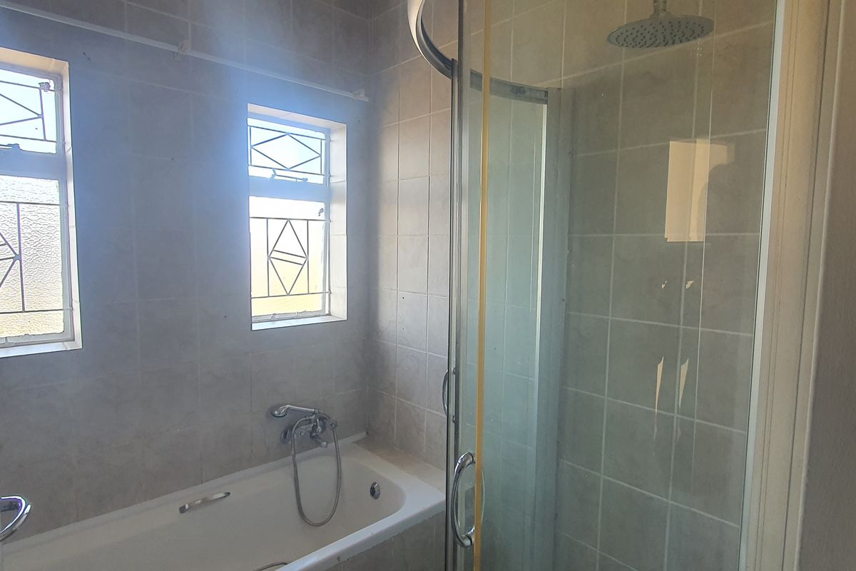 A functional bathroom featuring a built-in bathtub, a separate glass-enclosed shower, and tiled walls with natural light from two windows.