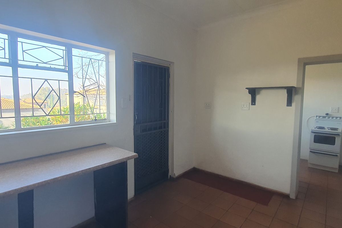 A functional kitchen and scullery area featuring tiled flooring, built-in countertops, and a separate prep space with a stove.