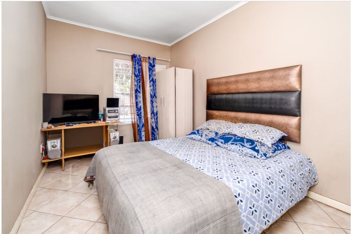 A standard bedroom featuring tiled flooring and a window fitted with security bars.