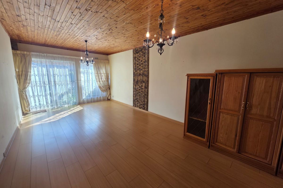 Spacious living area featuring wood-paneled ceilings, laminate flooring, and a decorative stone wall accent, leading to a bright patio through sliding glass doors.