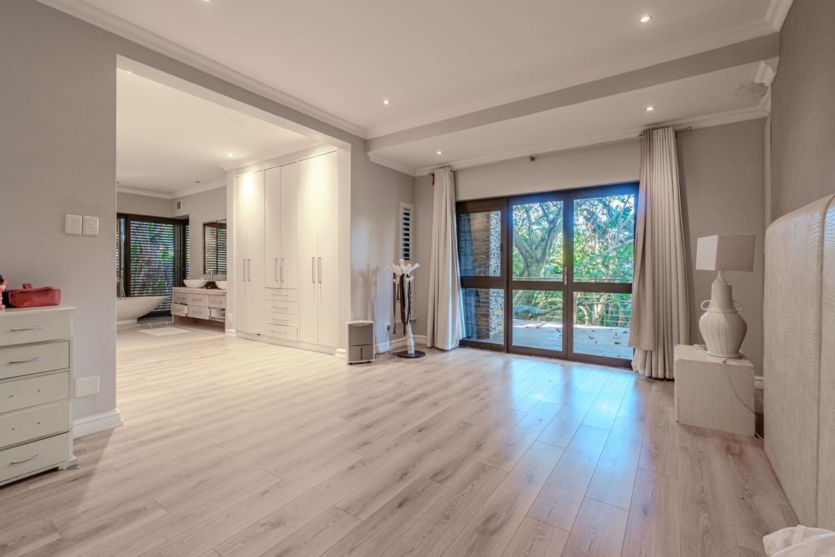 Spacious bedroom featuring light laminate flooring, extensive built-in cabinetry, recessed lighting, and sliding glass doors leading to an outdoor area.