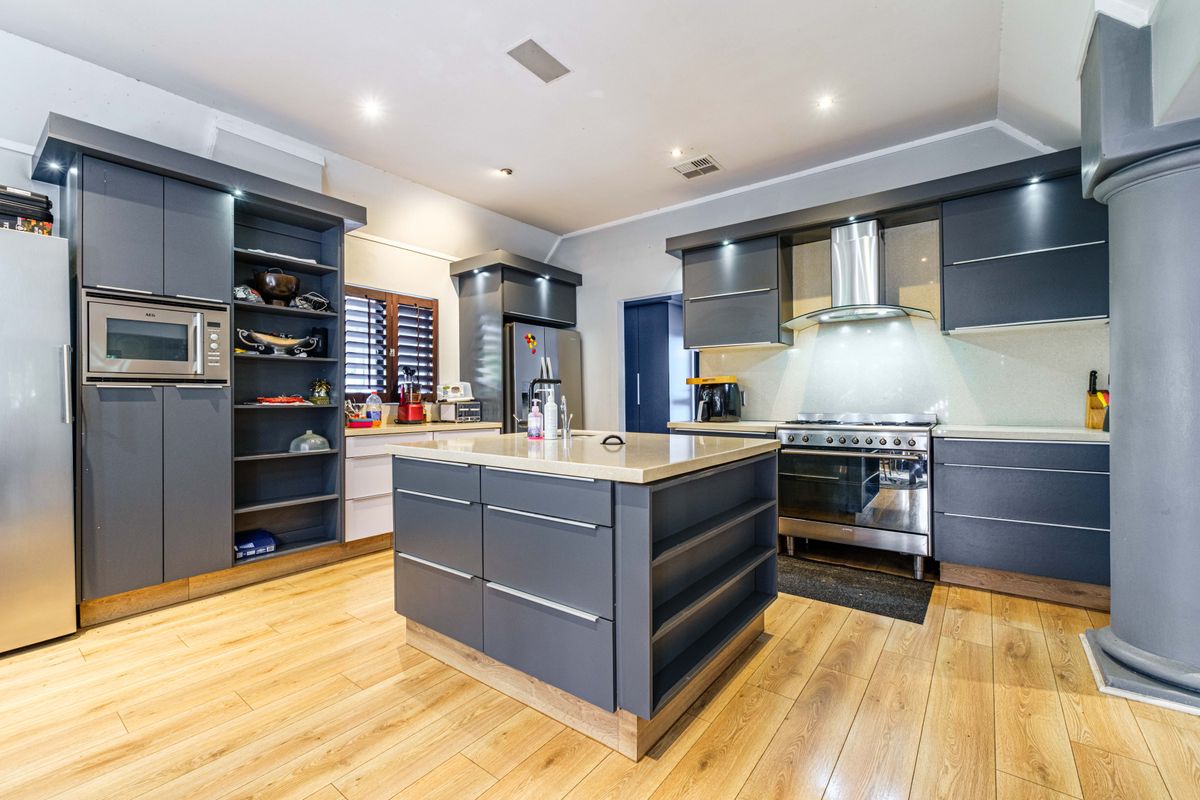Modern kitchen featuring dark grey cabinetry, a central island with stone countertops, stainless steel appliances, and warm timber flooring.