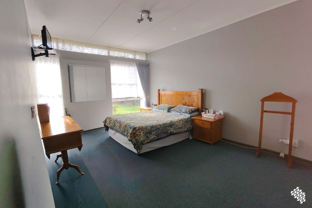 Spacious bedroom featuring large windows with natural light, neutral wall finishes, and fitted carpeting.