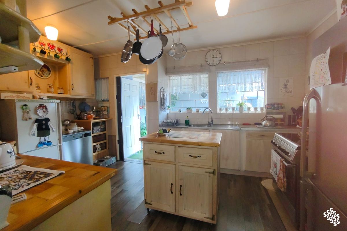 A functional kitchen featuring wooden cabinetry, a central island, stainless steel sink, and a freestanding oven, with direct access to the exterior.