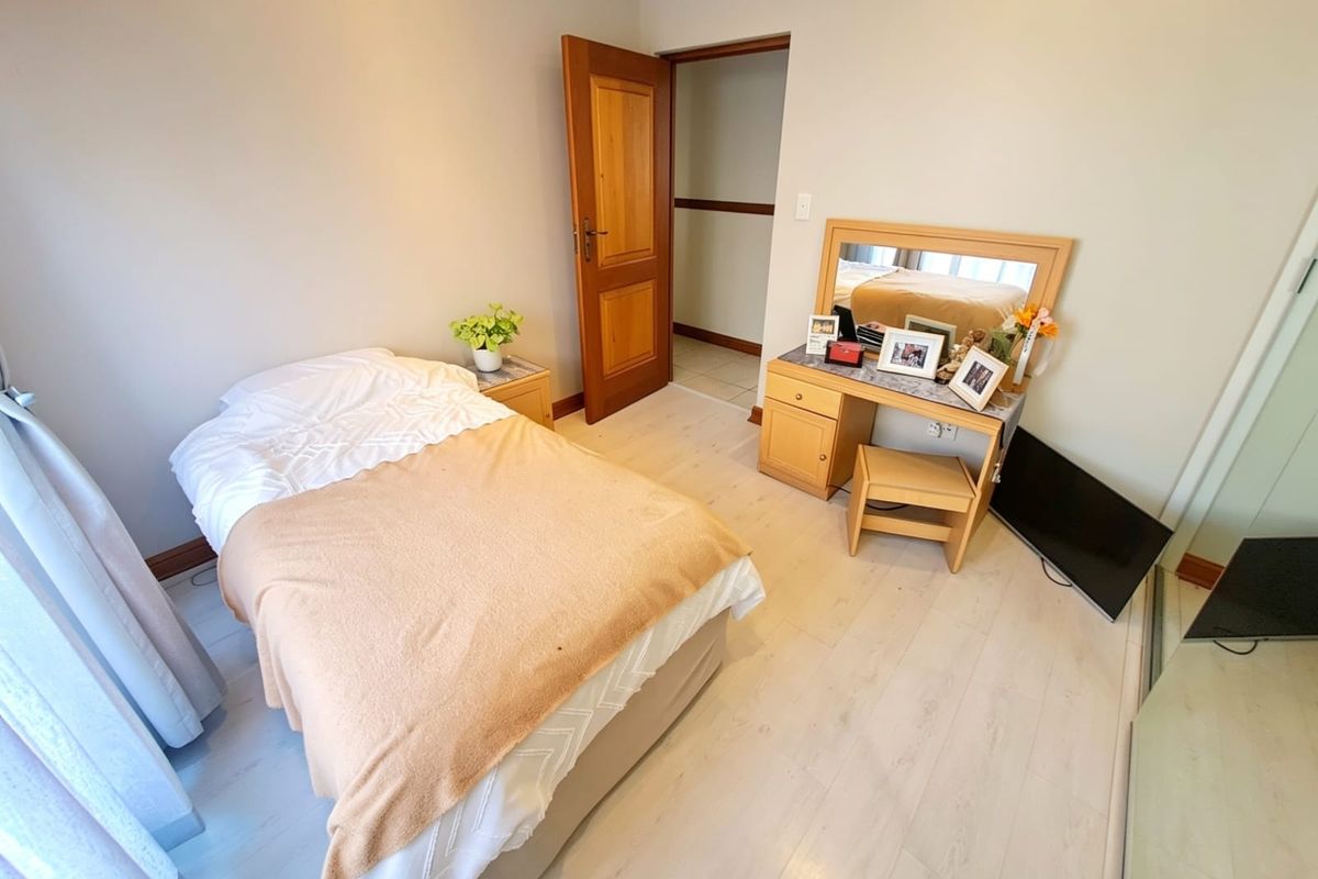 A functional bedroom featuring light-toned laminate flooring, neutral wall finishes, and a solid timber door leading to an adjacent space.