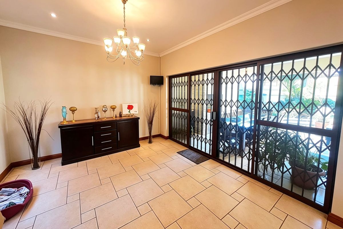 Spacious living area featuring large sliding glass doors with security gates, tiled flooring, and recessed downlighting, providing seamless access to the outdoor patio.