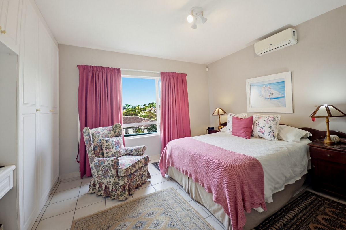 A well-lit bedroom featuring built-in cupboards, tiled flooring, and a wall-mounted split-system air conditioner, offering a comfortable living space with exterior views.