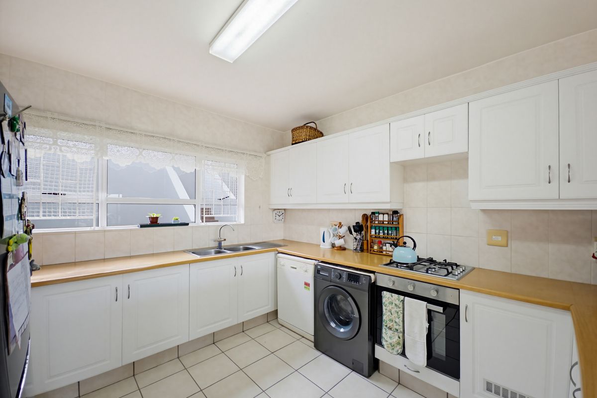 A functional kitchen featuring white cabinetry, laminate countertops, tiled backsplash, and integrated gas hob and oven, providing a clean and practical workspace.