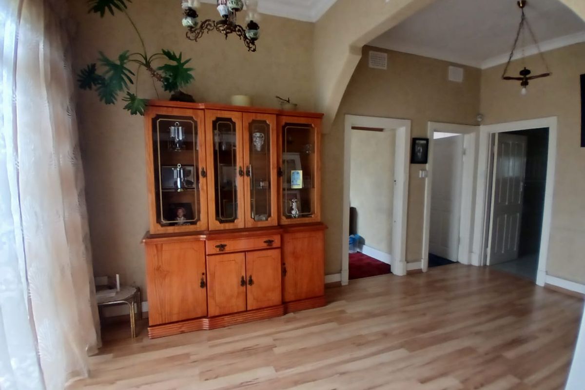 A living area featuring light timber-look flooring, decorative ceiling cornices, and multiple doorways leading to adjacent rooms.