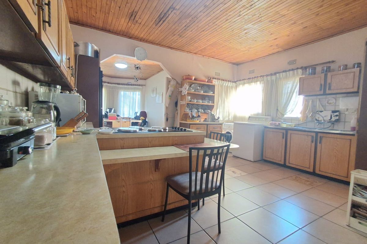 Spacious kitchen featuring timber cabinetry, a central island with a built-in hob, and tiled flooring, opening into an adjacent living area.