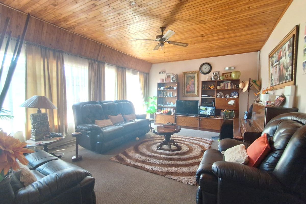 A spacious living room featuring a distinctive wood-paneled ceiling, large windows allowing natural light, and carpeted flooring.