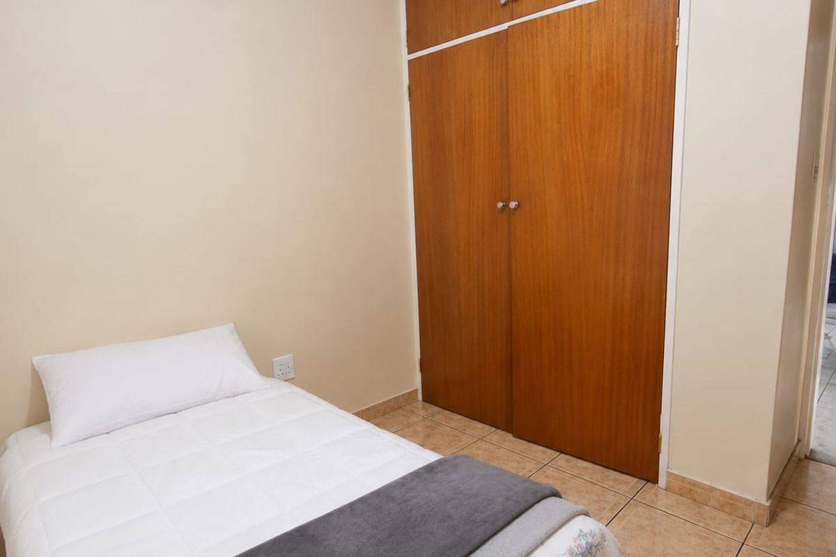 A compact bedroom featuring built-in wooden cupboards and tiled flooring, offering a functional and neutral living space.