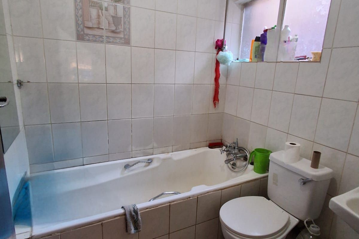 A compact bathroom featuring a standard bathtub, toilet, and wall-mounted basin with dated ceramic tiling throughout.