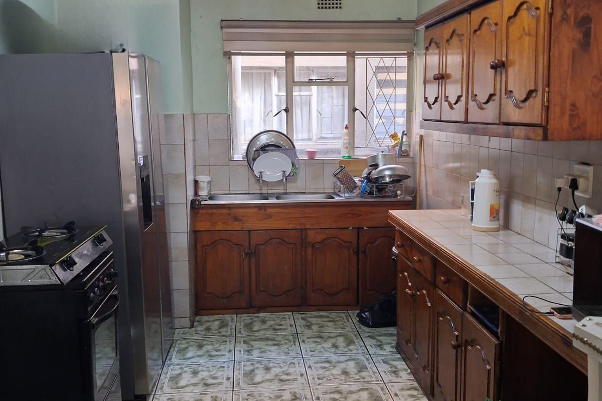 A functional kitchen featuring traditional wooden cabinetry, tiled countertops, and a double basin sink with a window view.