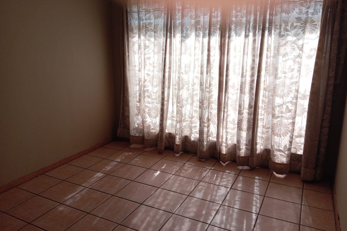 An empty bedroom featuring ceramic floor tiles and large windows covered by floral curtains, offering a blank canvas for potential interior design.