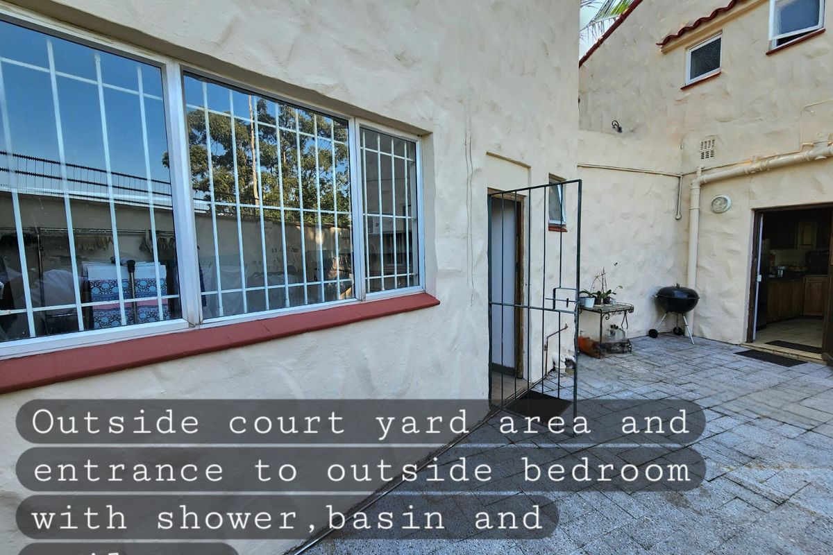 A paved rear courtyard area featuring an entrance to an external bedroom suite with integrated bathroom facilities.