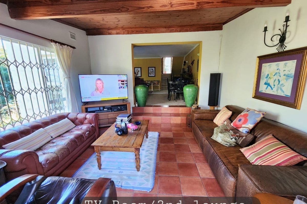 A cozy second lounge or TV room featuring exposed timber ceiling beams, terracotta floor tiles, and a raised step leading to an adjacent dining area.