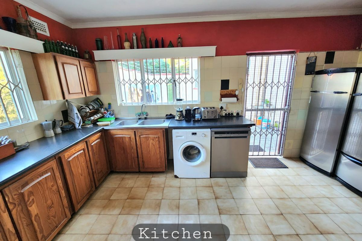 Functional kitchen featuring wooden cabinetry, double basin sink, tiled flooring, and direct access to an exterior area through a security gate.