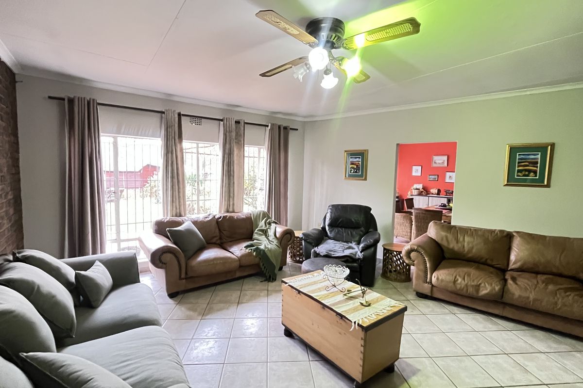 Spacious living room featuring tiled flooring, a brick feature wall, and large windows with security bars, leading into an adjacent dining area.
