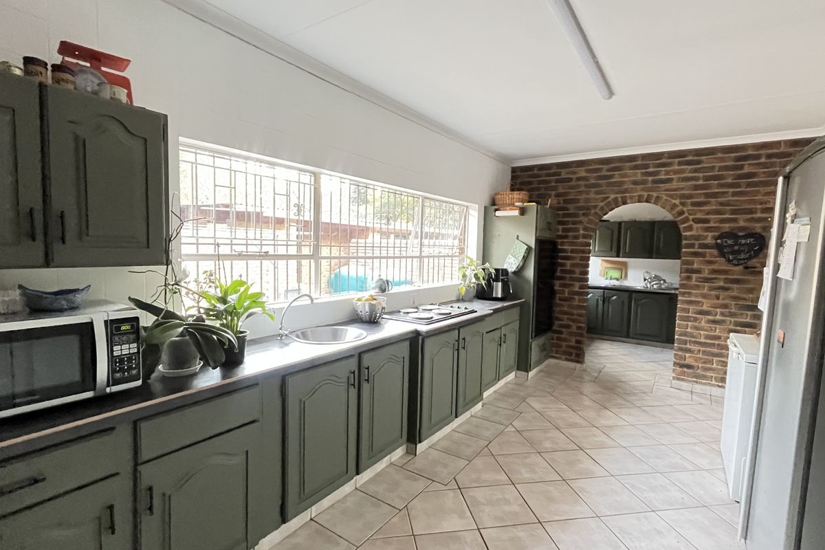 Spacious kitchen featuring olive green cabinetry, a built-in hob, and a brick archway leading to a secondary scullery area with tiled flooring.
