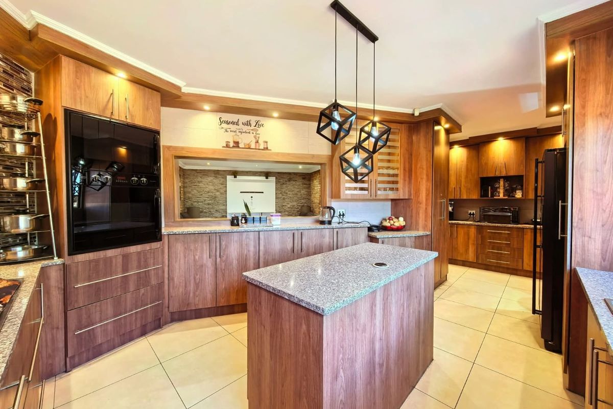 A well-appointed kitchen featuring warm wood-toned cabinetry, granite countertops, a central island, and modern pendant lighting with a convenient pass-through window.