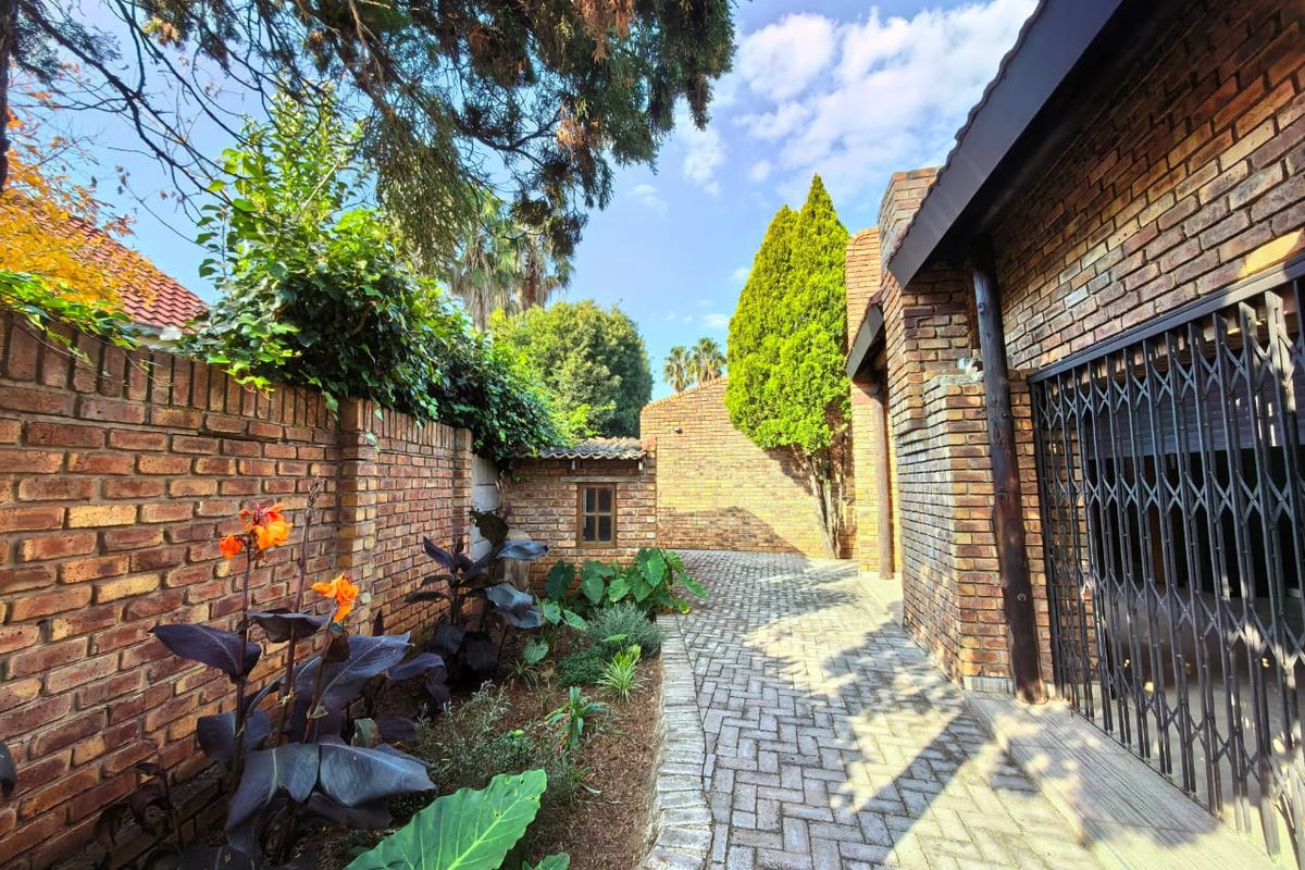 A well-maintained rear courtyard featuring exposed brick walls, paved pathways, and established garden beds alongside a secure entrance.