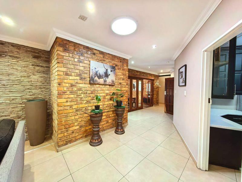 Spacious hallway featuring an exposed brick feature wall, stone cladding accents, tiled flooring, and elegant coved cornicing leading to adjacent living areas.