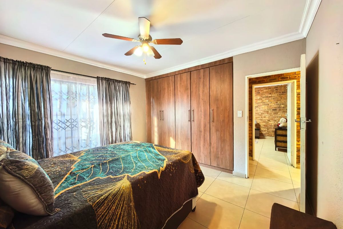 A well-maintained bedroom featuring built-in wooden cupboards, tiled flooring, and a ceiling fan, with direct access to an adjacent room.