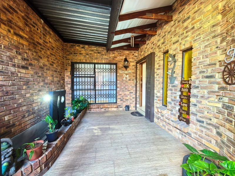 A covered entrance patio featuring exposed brick walls, tiled flooring, and timber roof rafters, providing a welcoming and secure entry area.