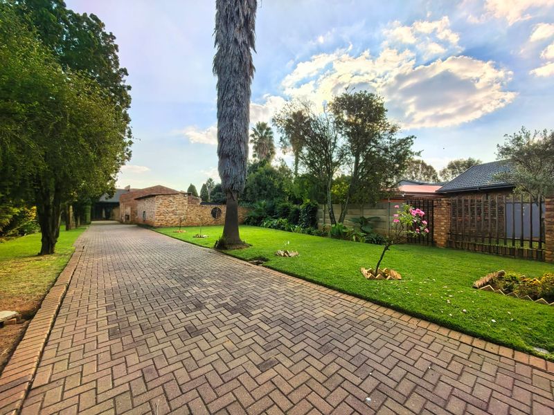 A well-maintained front garden featuring a long paved driveway, manicured lawn, and established brick boundary walls.
