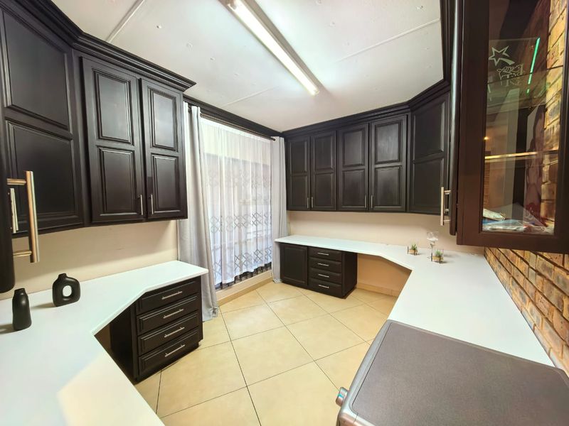A functional scullery or utility area featuring dark wood cabinetry, ample white countertop workspace, tiled flooring, and an exposed brick feature wall.