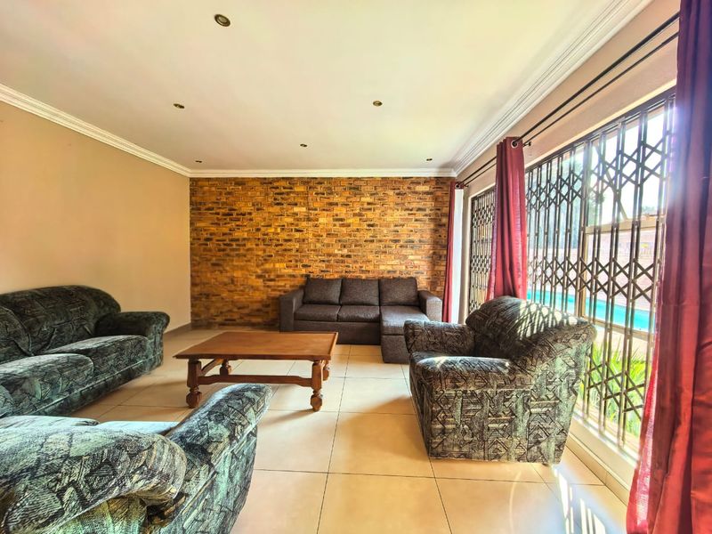 Spacious living room featuring an exposed brick accent wall, tiled flooring, and large sliding doors with security gates leading to the outdoor area.